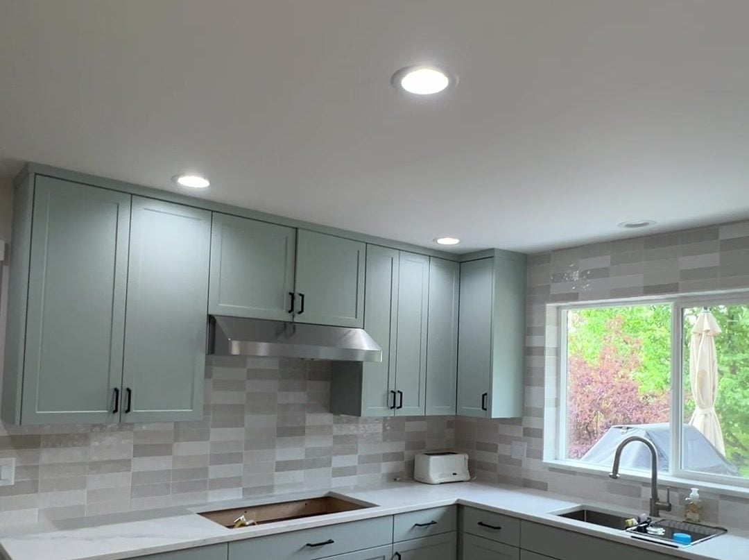 Sage green painted kitchen cabinets with black pulls and a gray tile backsplash