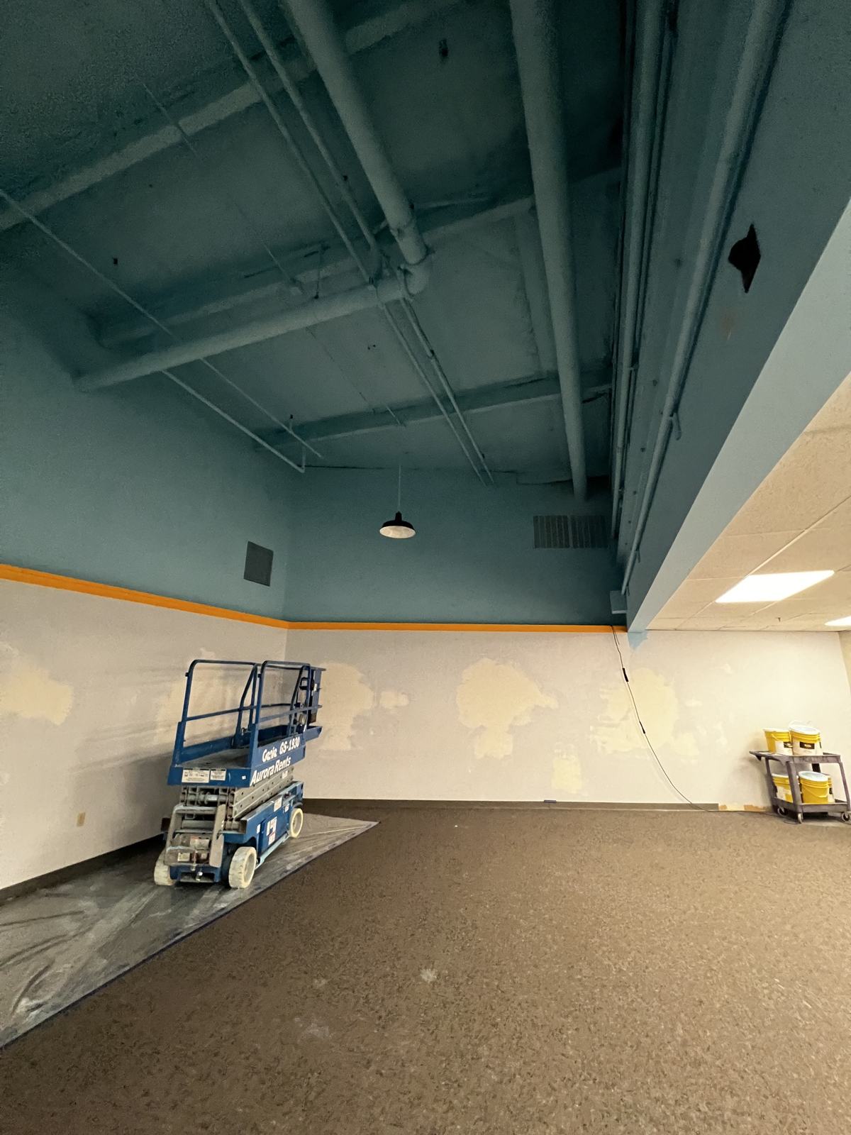 Scissor lift on a protected floor during a commercial ceiling repaint in a church