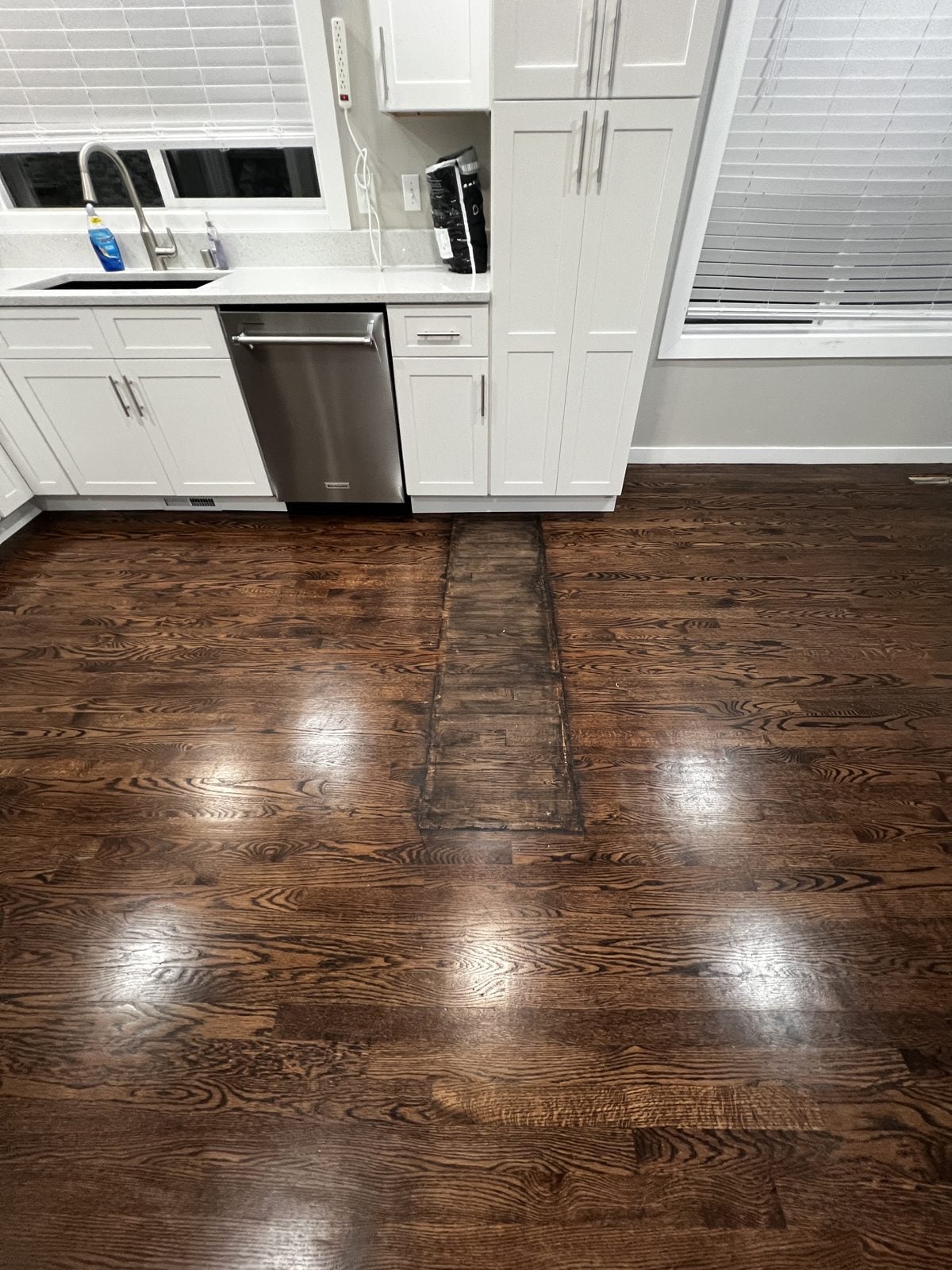 Worn hardwood kitchen floor with a mismatched patched strip