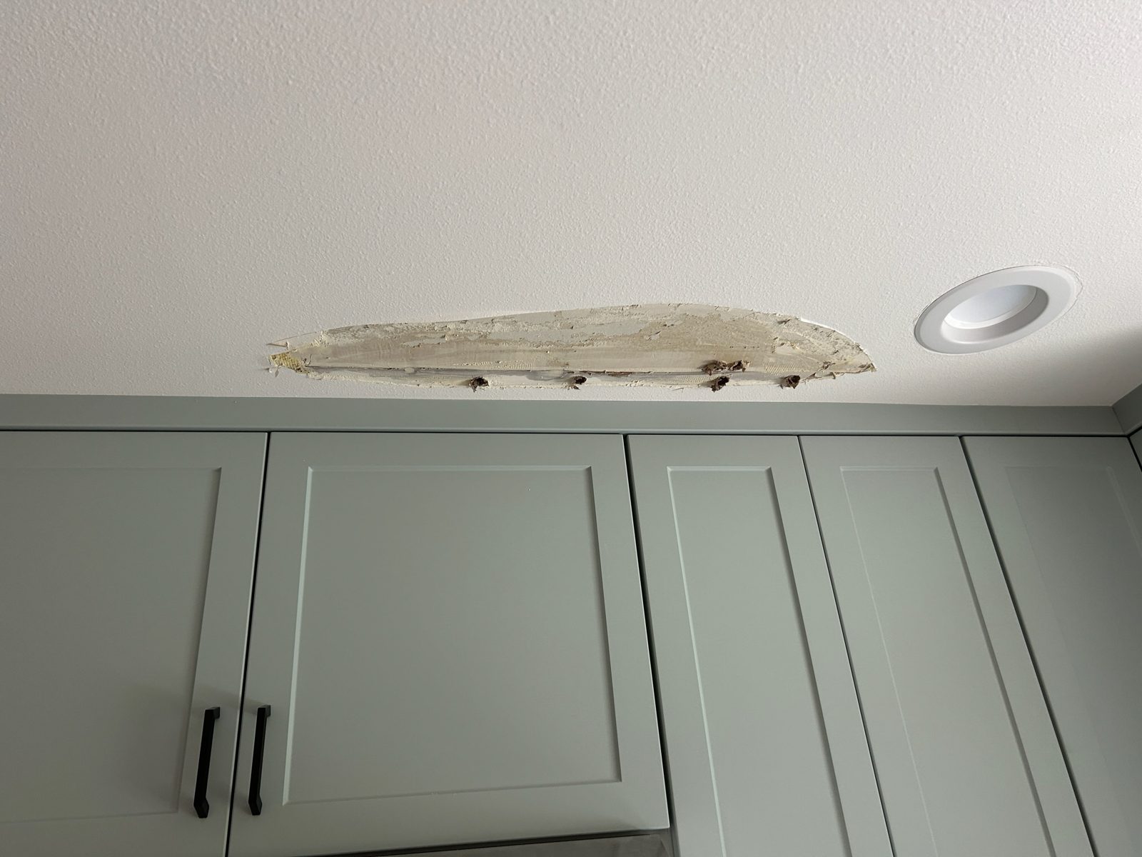 Water-damaged ceiling drywall being repaired above kitchen cabinets