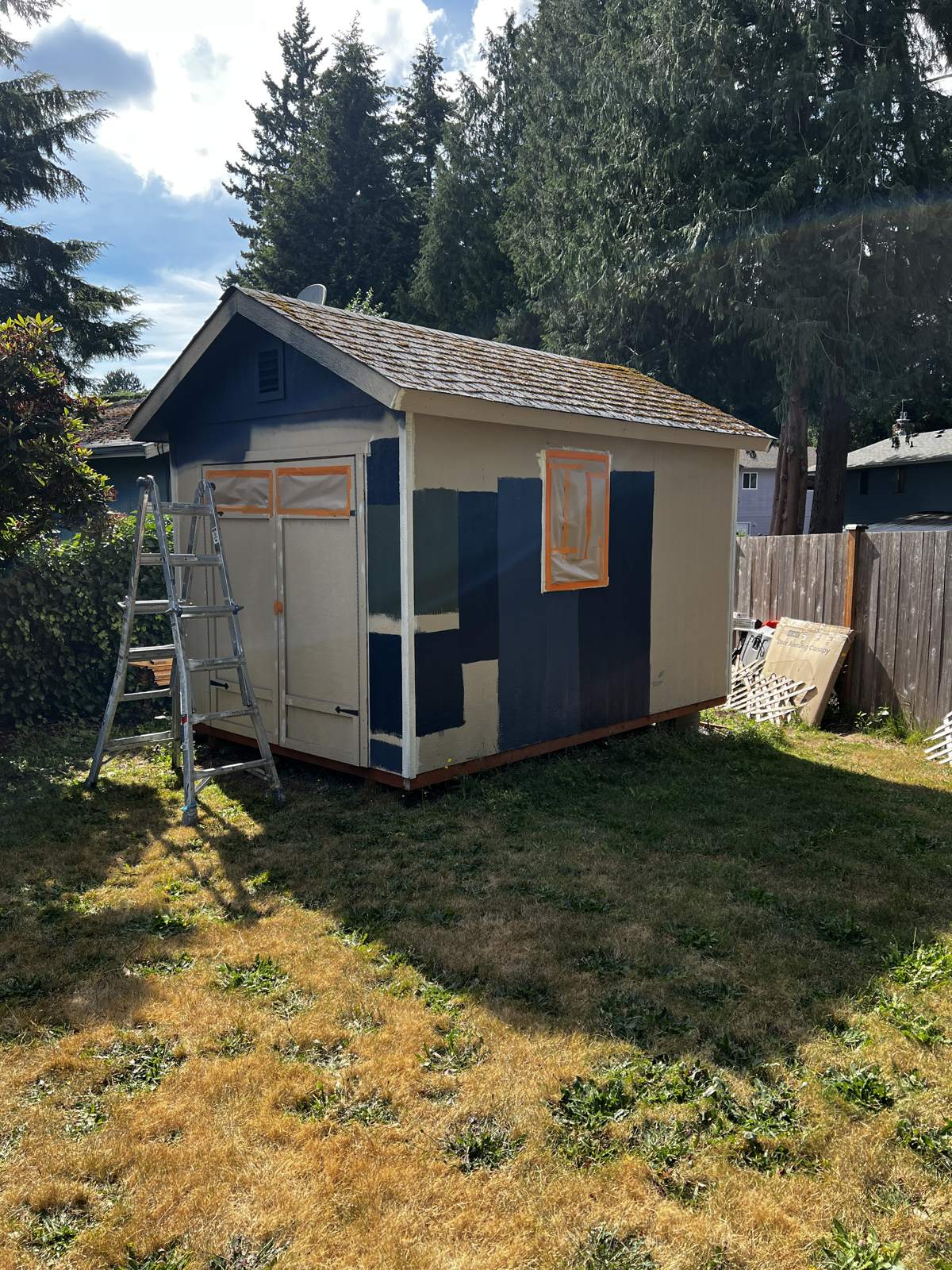 Tan shed with navy color samples painted on the siding